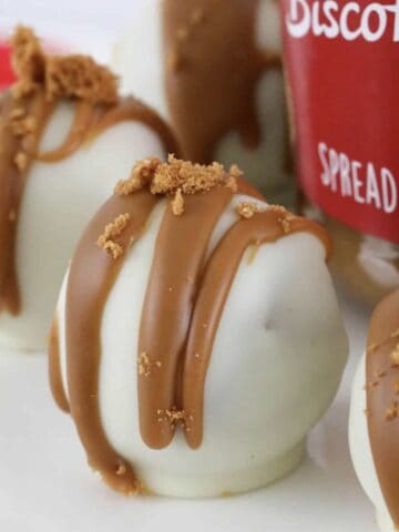A close up shot of a truffle coated in white chocolate and drizzled with Biscoff.