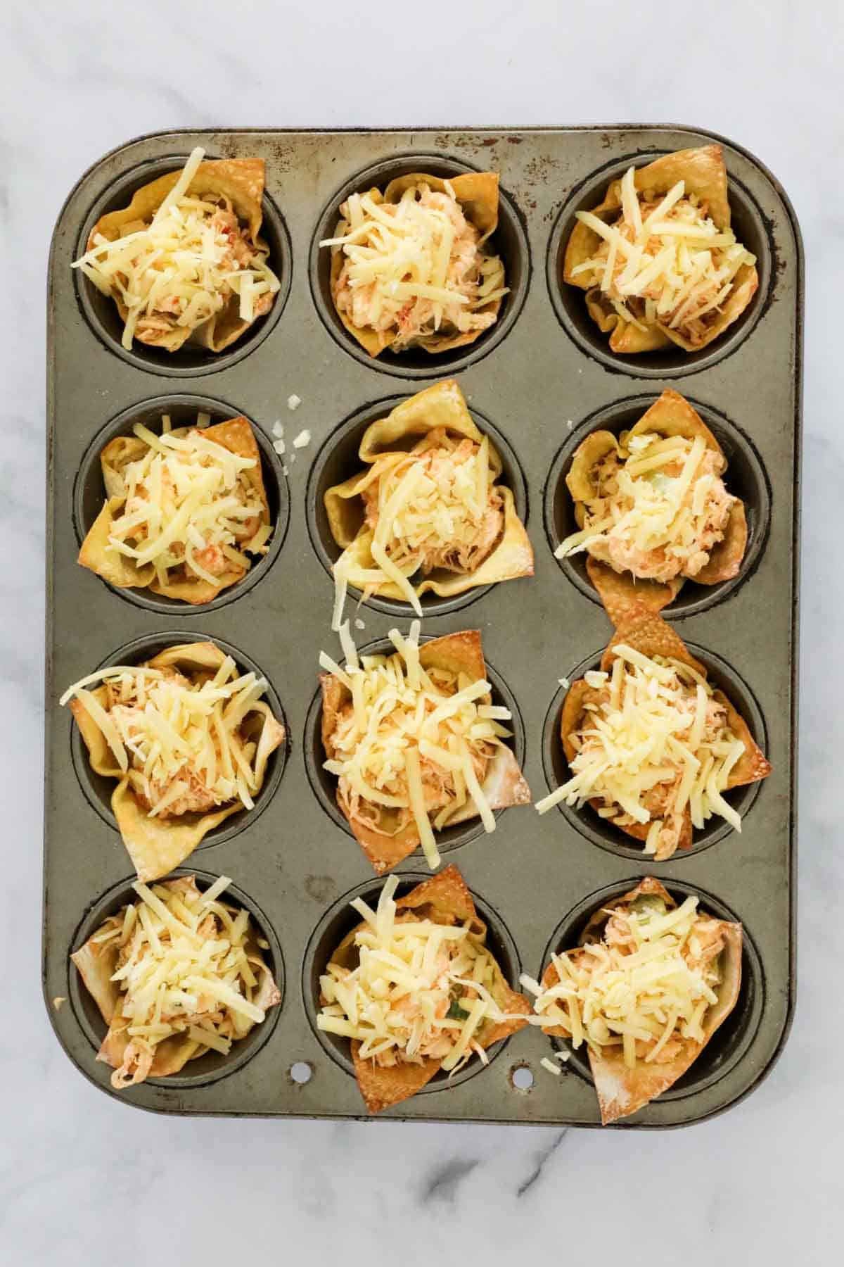 Crispy bases filled with mixture and sprinkled with cheese, ready to be baked.
