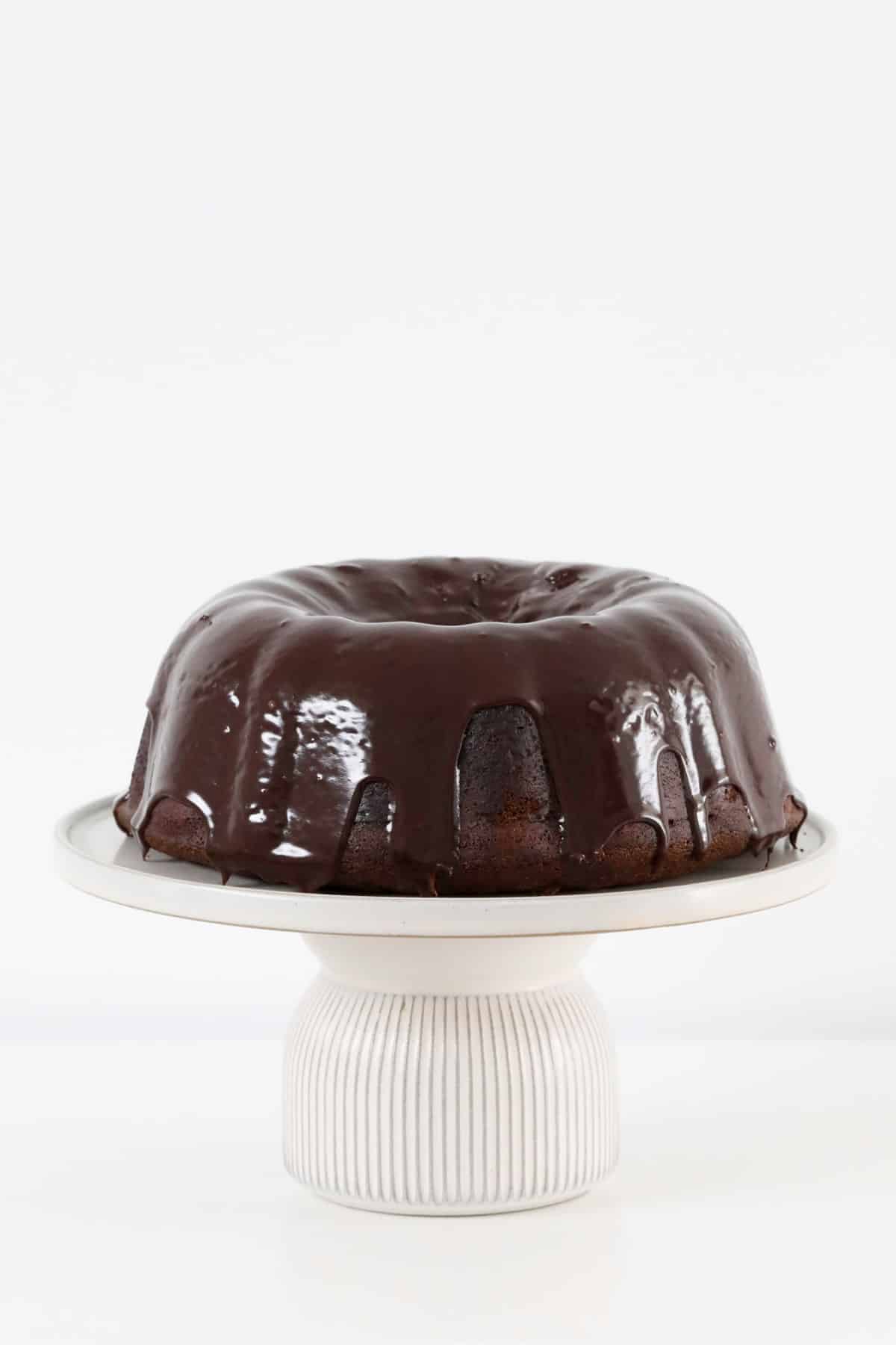 A ganache covered chocolate pound cake on a cake stand.