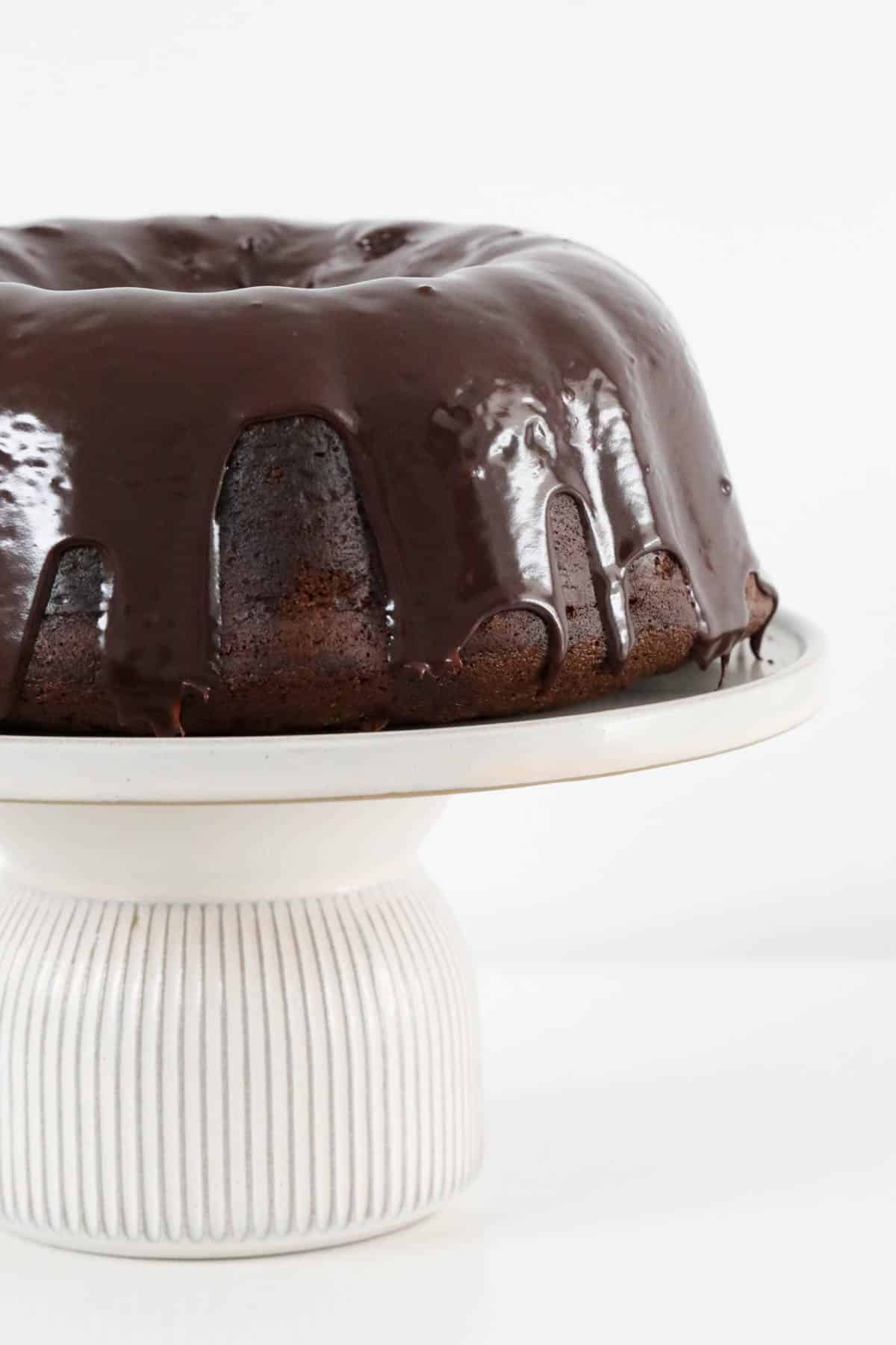 chocolate sour cream pound cake on a cake stand with chocolate ganache drizzled over the top.