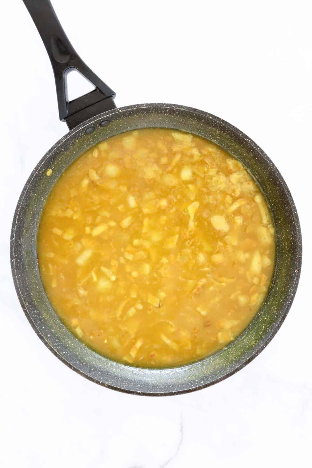 Cooked onions in a spicy sauce being brought to a simmer in a frying pan.