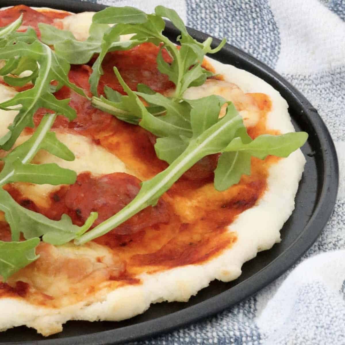 A gluten free rocket, cheese and pepperoni pizza on a baking tray.