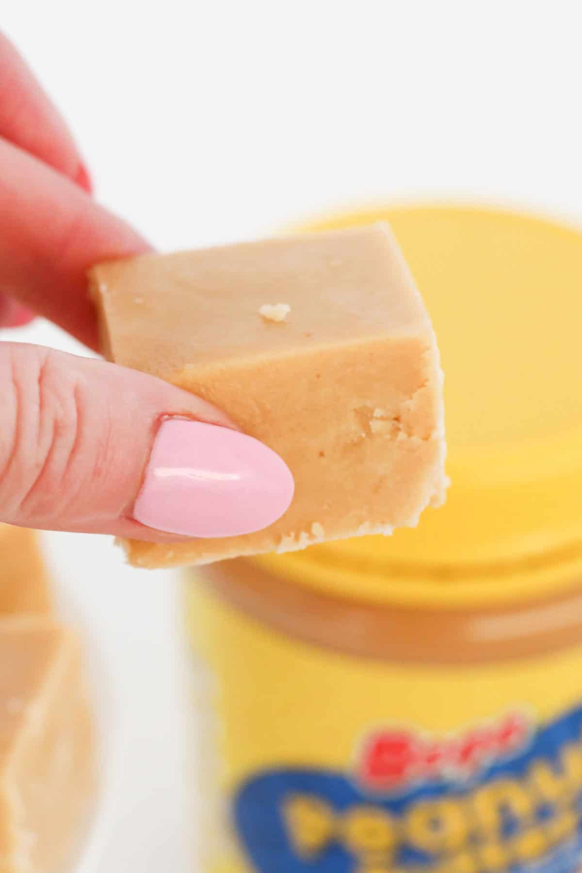 A hand holding a piece of caramel coloured fudge.