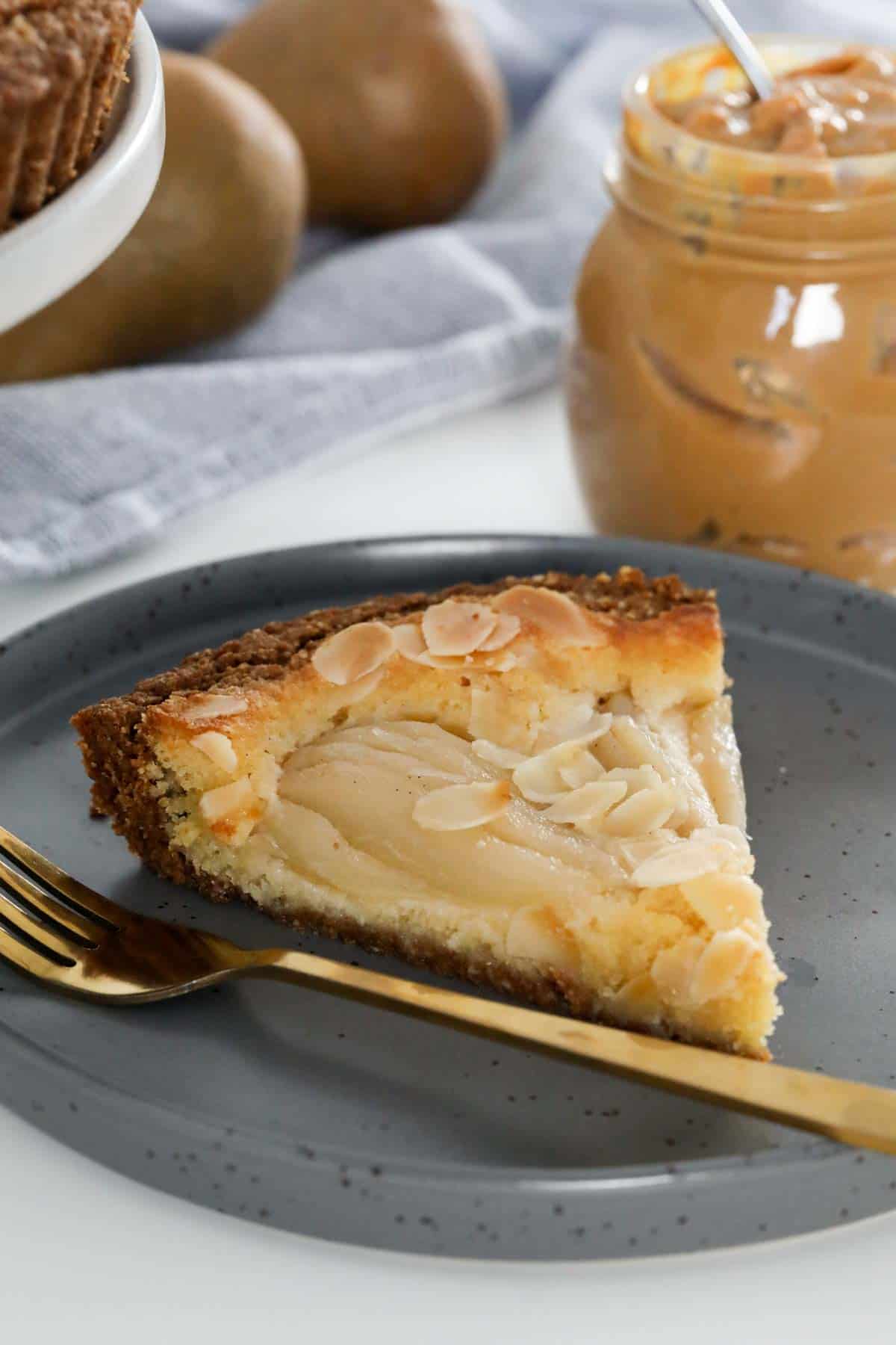A slice of frangipane pie on a plate with a gold fork.