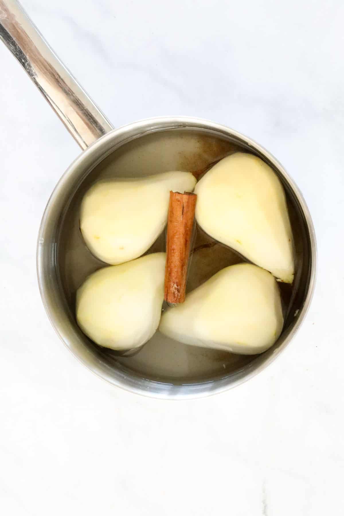 Peeled pears in a saucepan with cinnamon quills.
