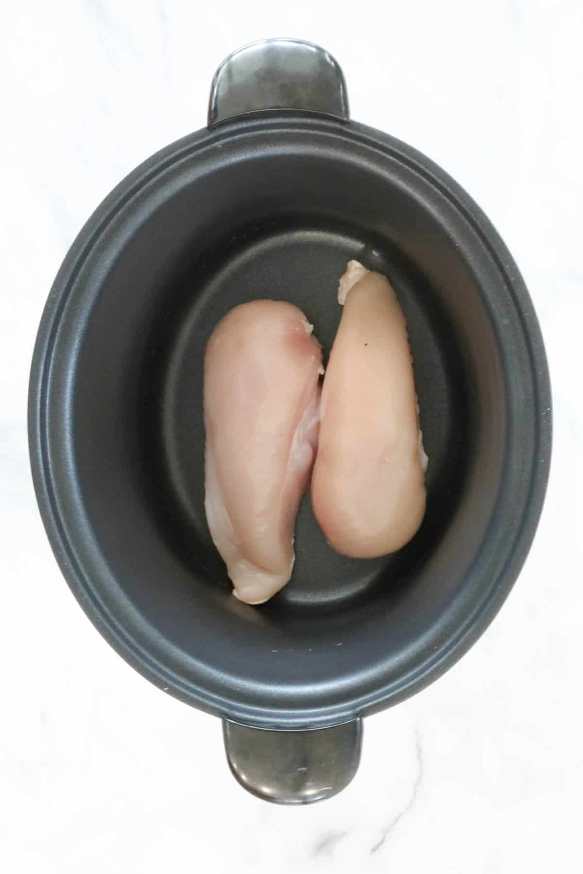 Two chicken breasts placed in a crock pot.