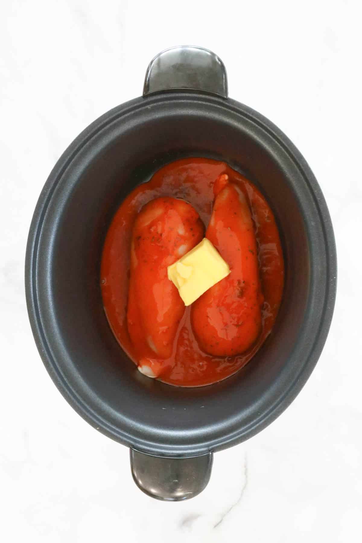 Red spicy sauce and butter on top of chicken in a slow cooker.