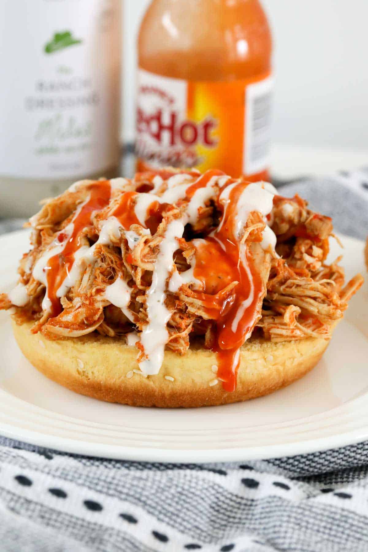 A hot sauce and ranch dressing drizzled over a shredded spicy chicken burger.