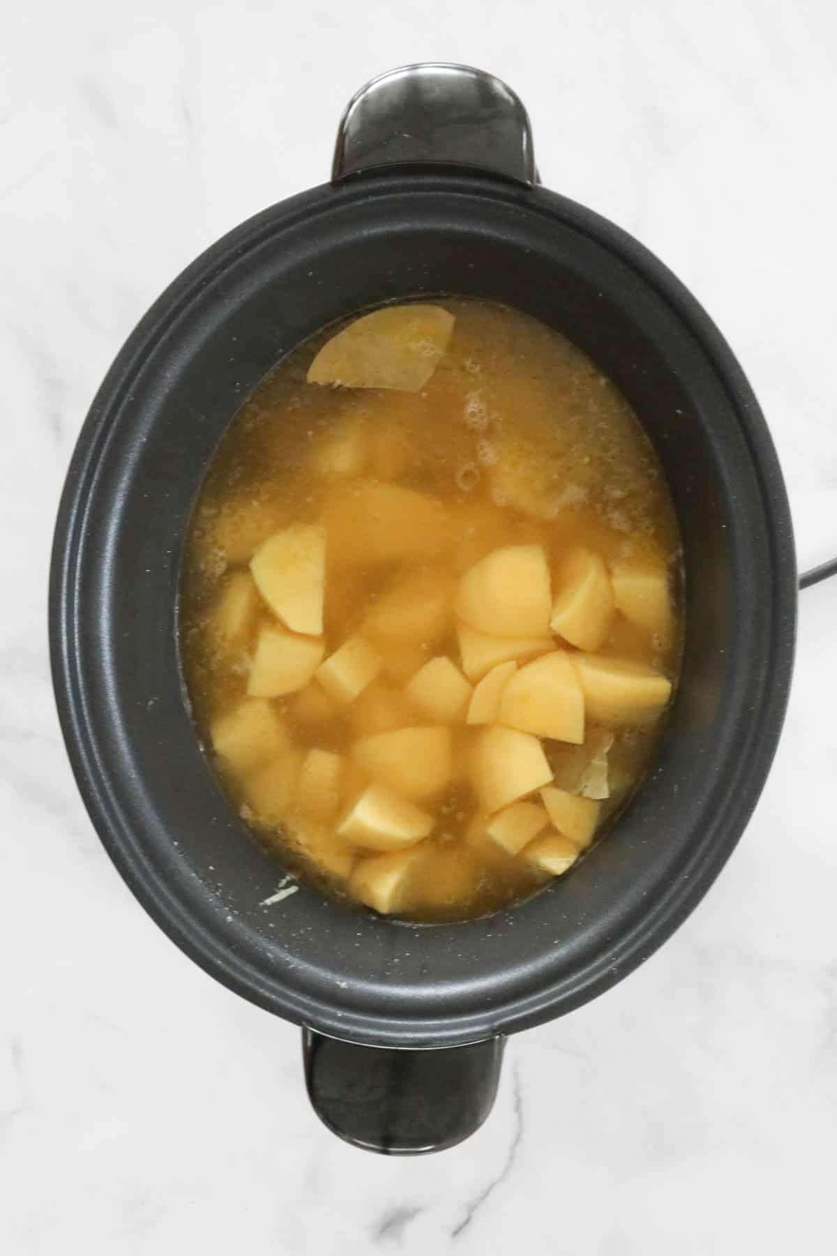 Chunks of potato and liquid stock added to the crock pot.