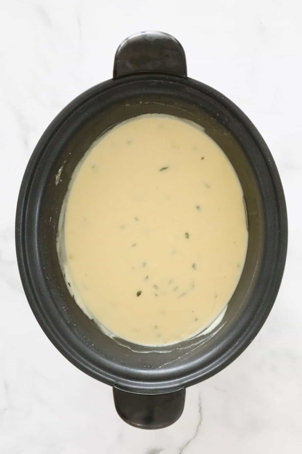 Creamy blended soup in a black slow cooker.