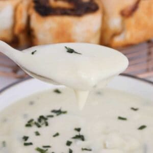 A spoon holding a creamy potato and leek soup with a bowl of soup underneath.