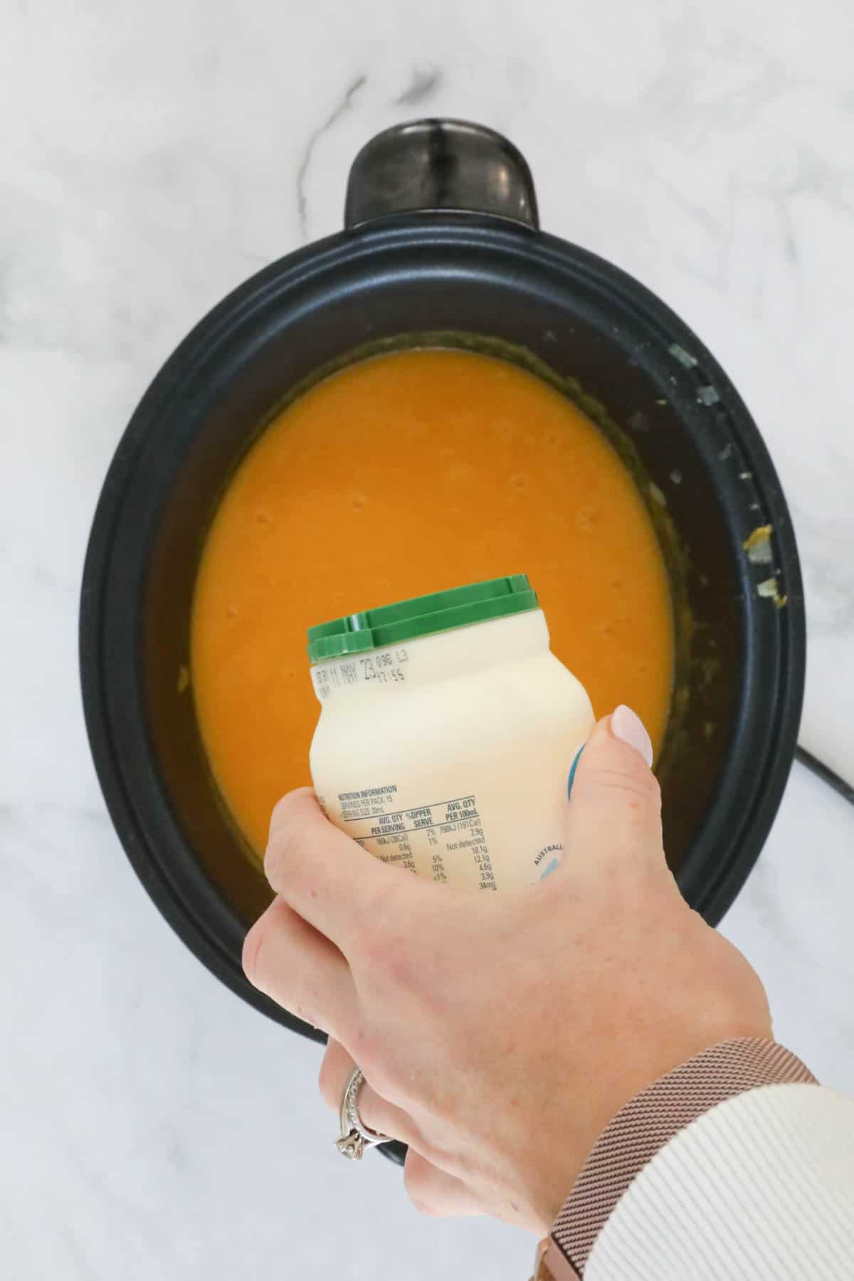 Cream being poured into a crock pot filled with soup.