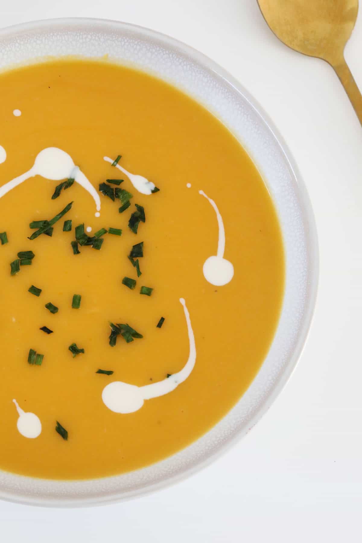 A bowl of pumpkin soup with a drizzle of cream and chopped chives to garnish.