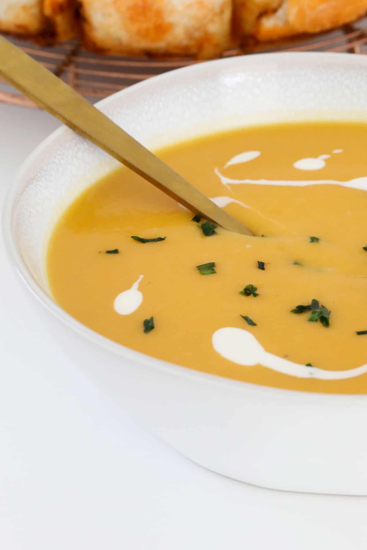 A white bowl filled with pumpkin soup and garnished with chopped chives.