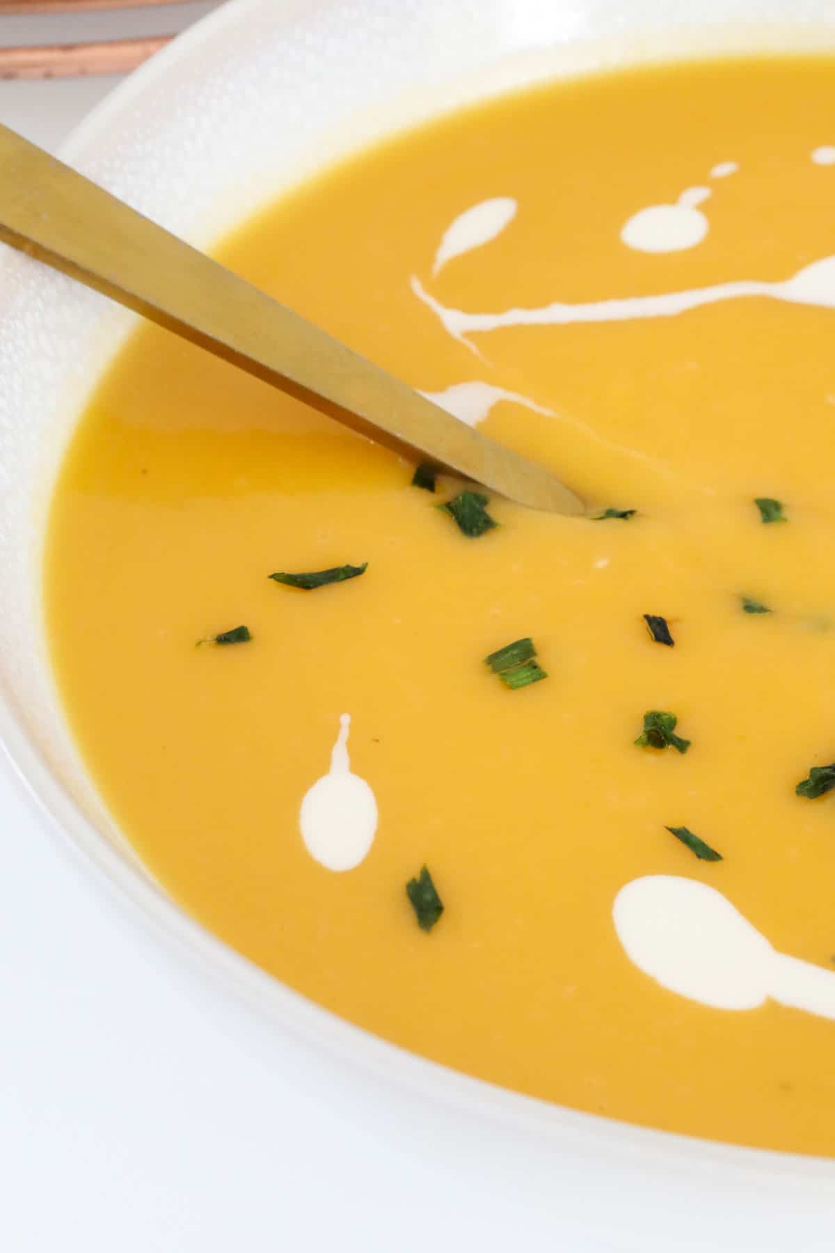 close up of chopped chives sprinkled on the top of an orange coloured soup.