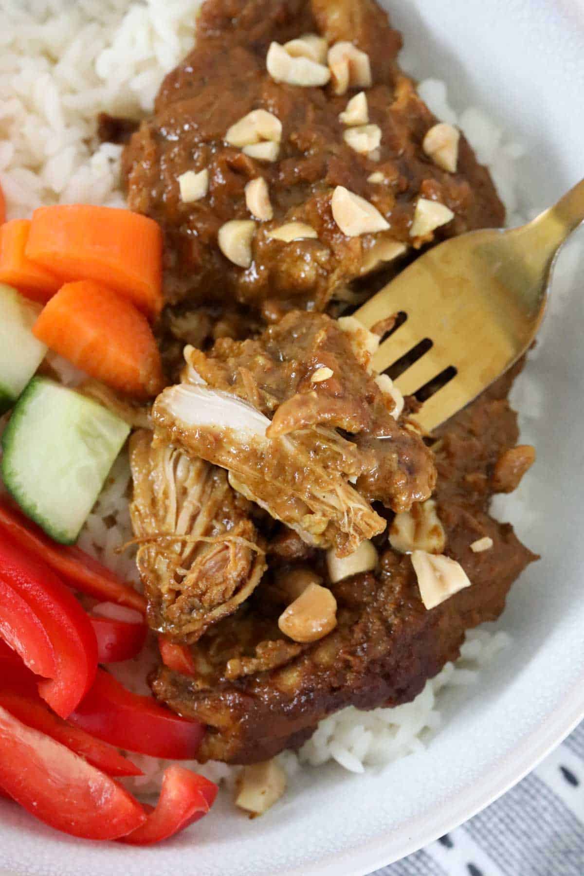 A bowl of slow cooker data chicken served with rice and fresh vegetables.