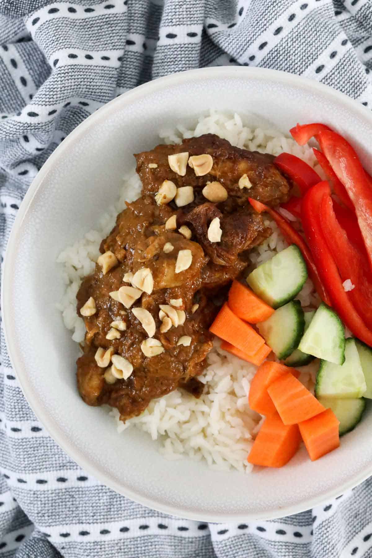 Satay chicken served with rice, raw carrot, cucumber and capsicum and sprinkled with peanuts.