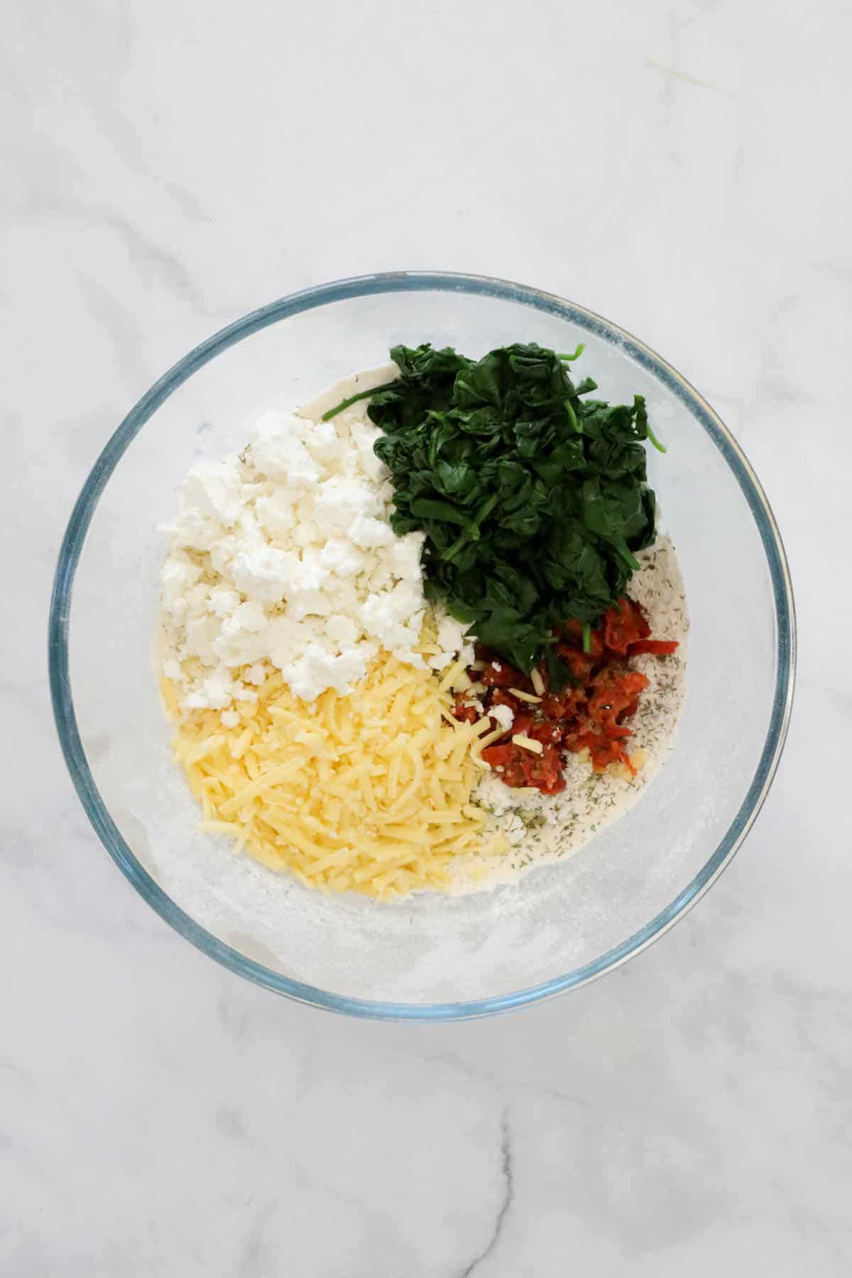 Drained spinach, feta cheese, grated cheese and sun dried tomatoes added to the flour in the mixing bowl.