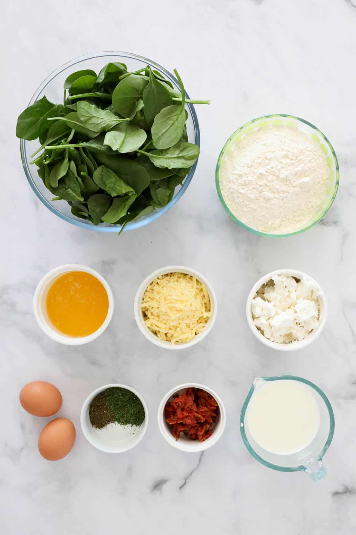 Ingredients needed to make spinach feta muffins weighed out and placed in individual bowls.