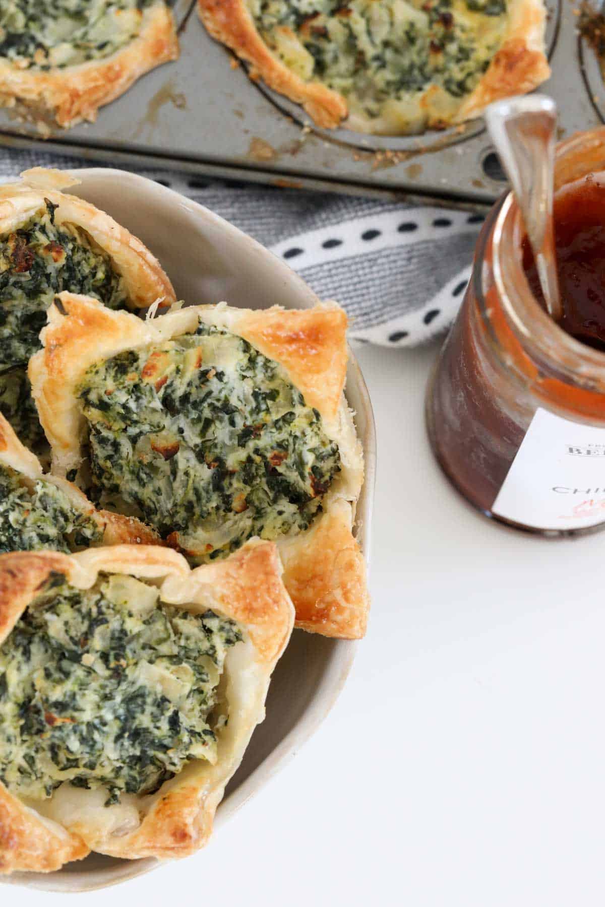 Ricotta and spinach pastries served with a jar of chutney nearby.