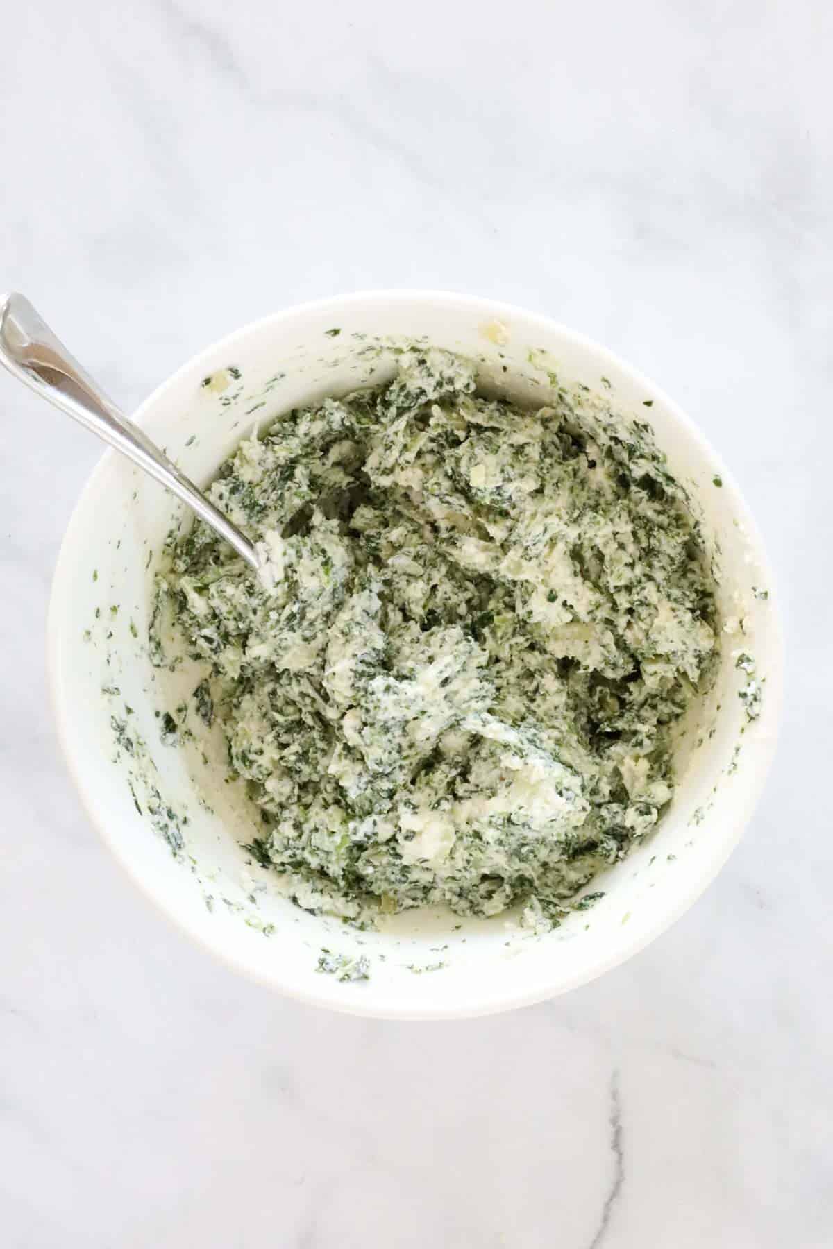 Thawed and drained spinach added to cheeses in a mixing bowl.