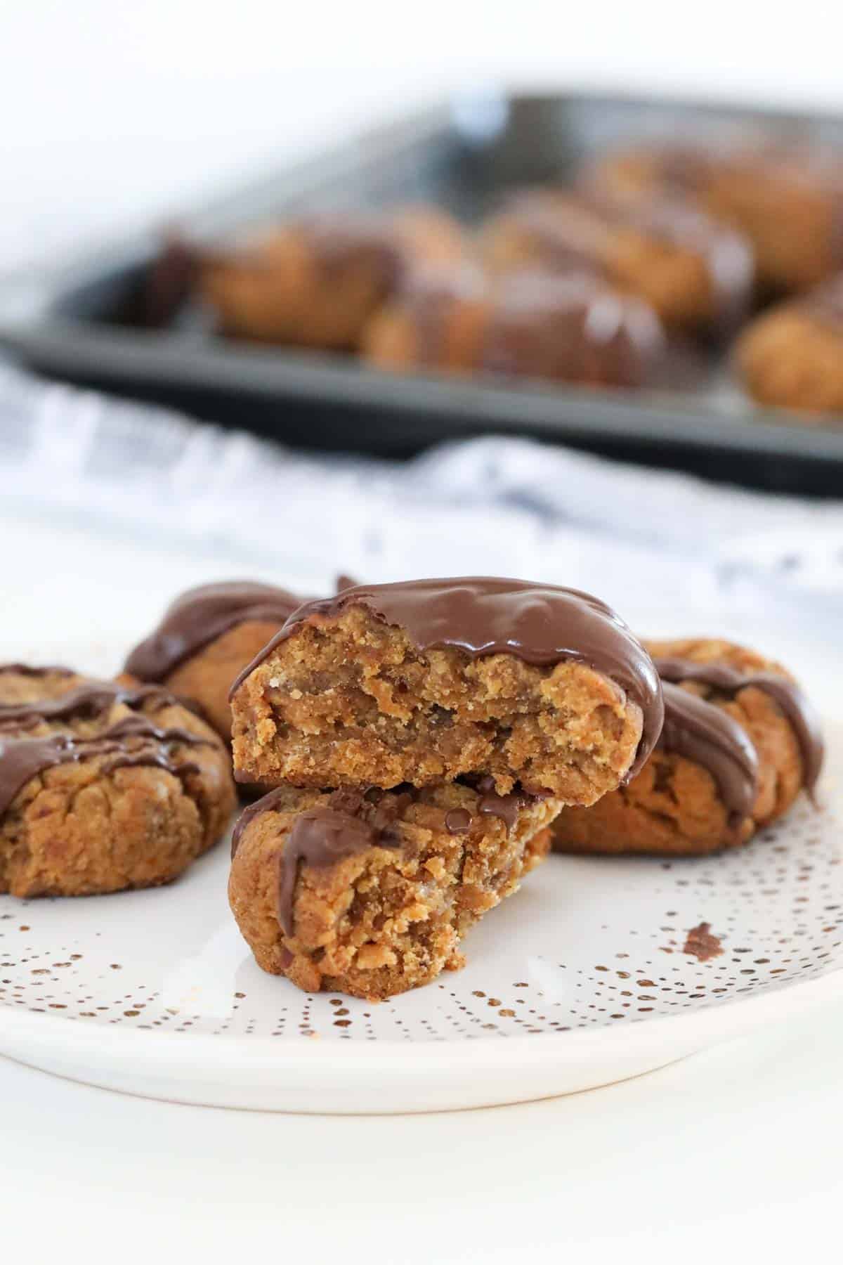 A plate of date cookies drizzled with chocolate, with one cookie broken in half to show the chewy centre.