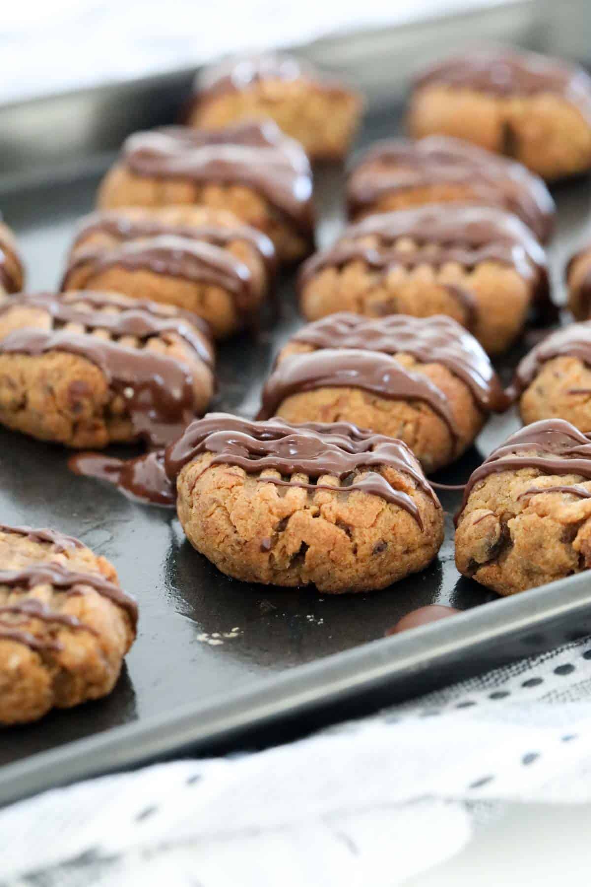 Date cookies on baking tray drizzled with melted chocolate.