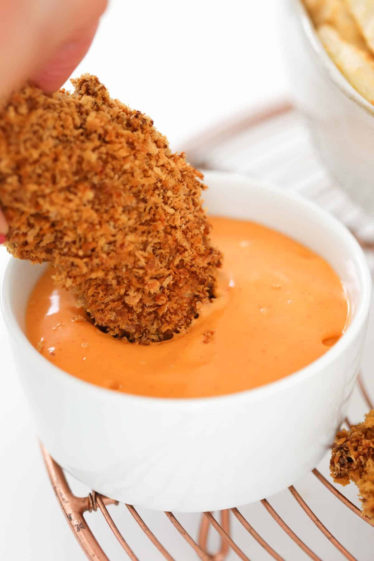 A baked chicken tenderloin being dipped in a bowl of spicy dipping sauce.