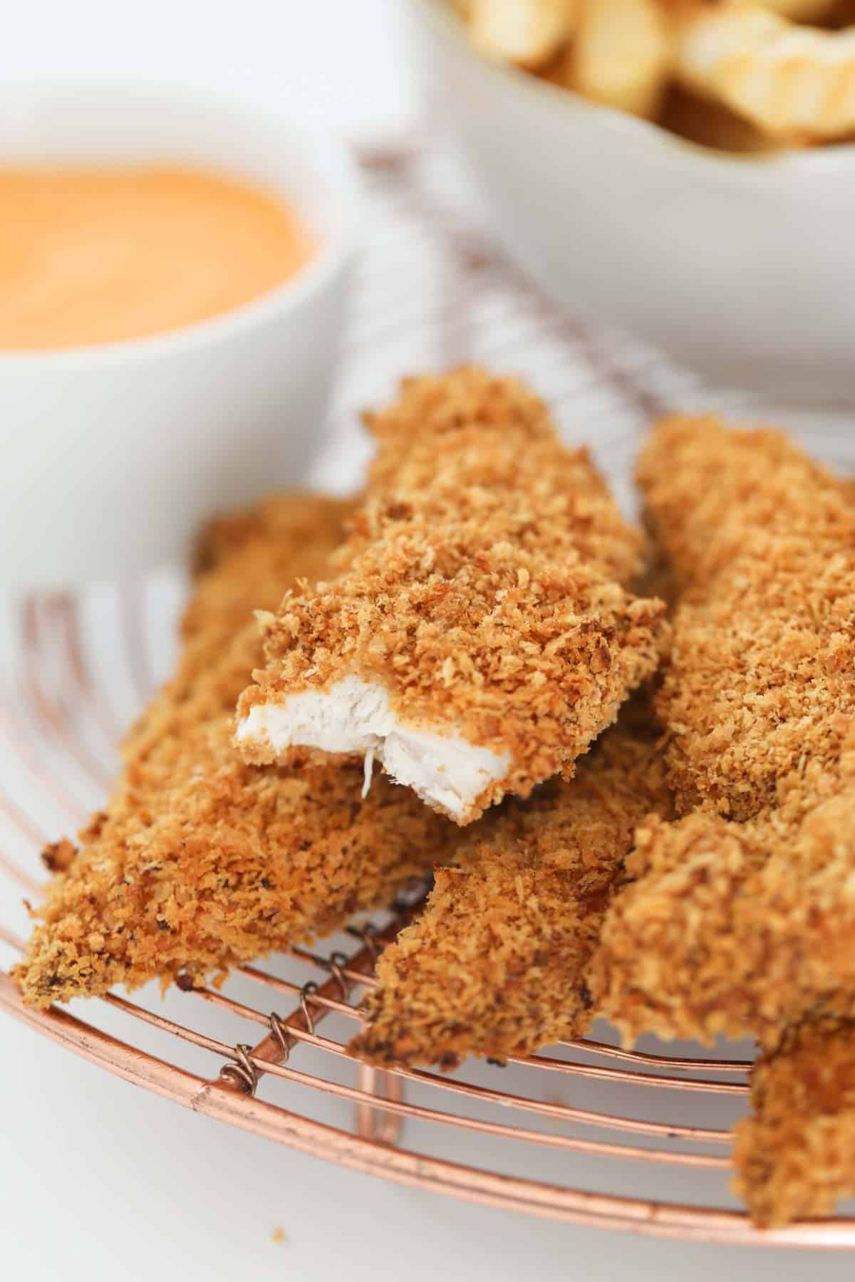 Crunchy breadcrumbed strips of baked chicken with a bite taken from one.