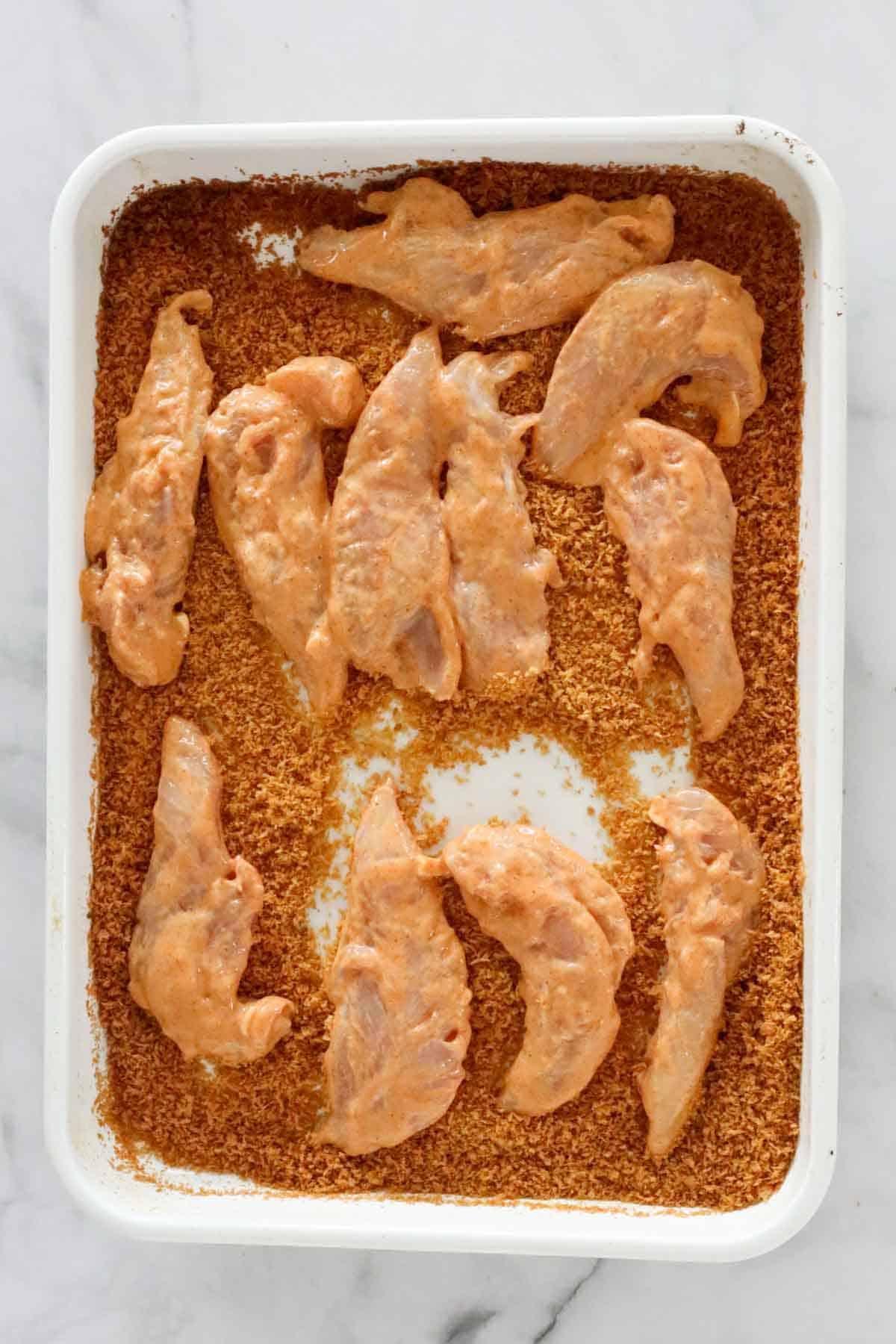 Seasoned tenderloins placed into a tray of toasted panko crumbs.