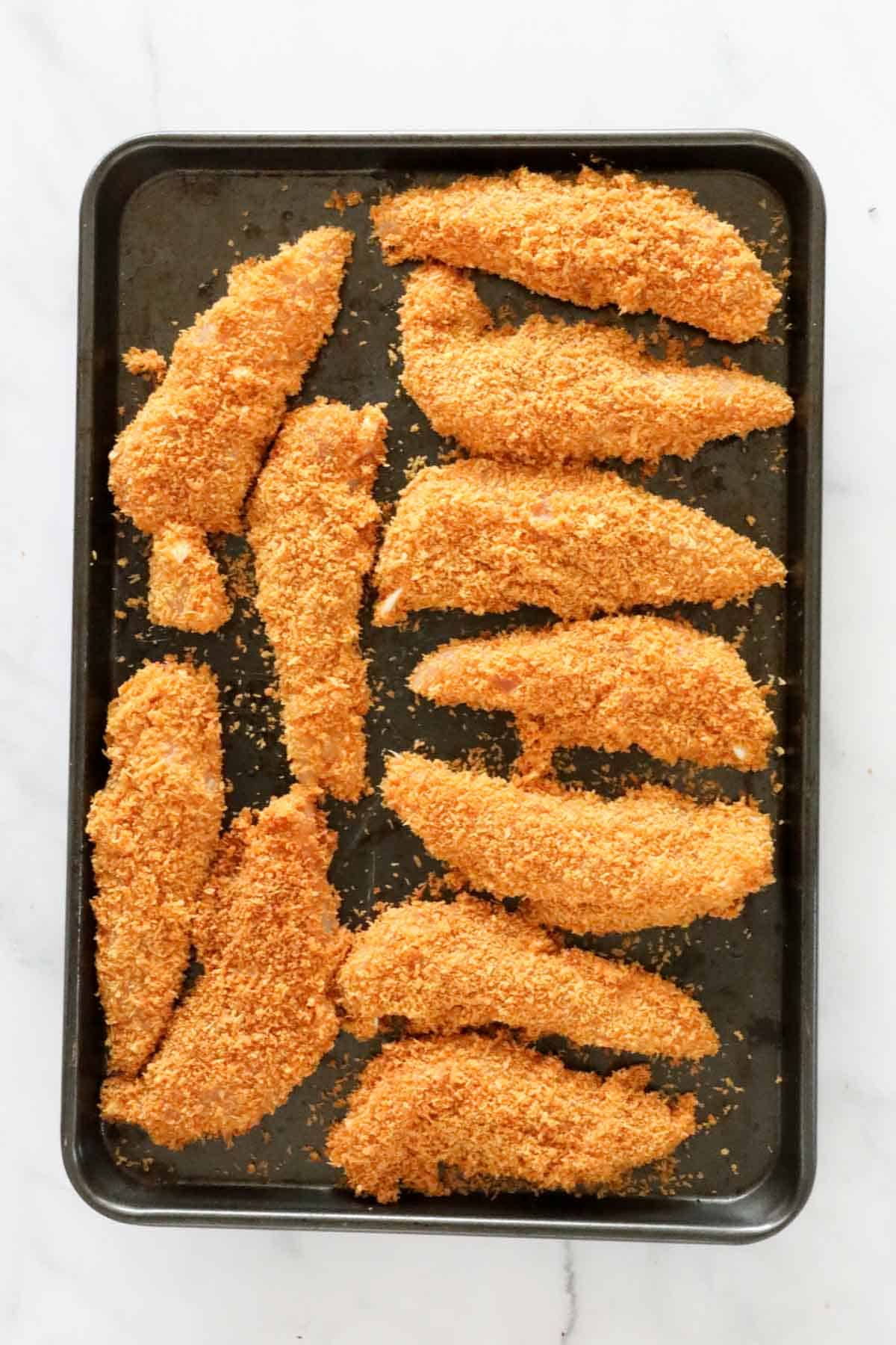 Baked chicken tenderloins on a baking tray.