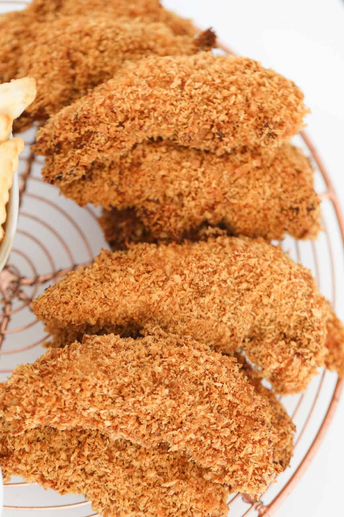 A close up of crispy breaded chicken tenders placed on a wire rack.