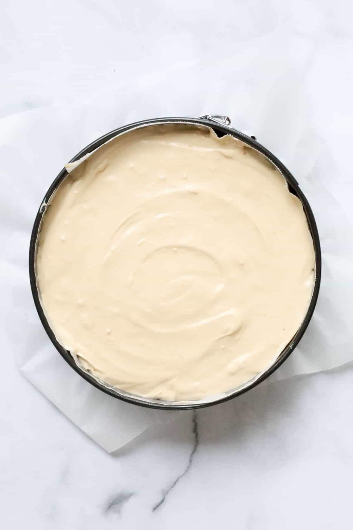 An overhead shot of a cream cheese filling spread in a springform tin.
