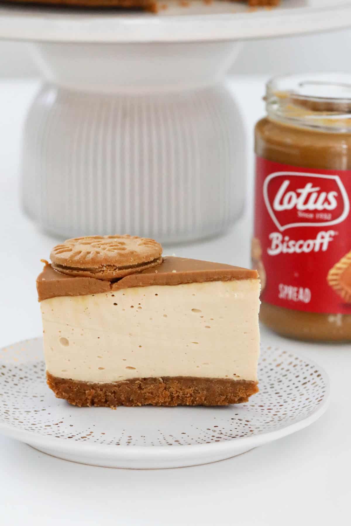 A slice of cheesecake with a jar of Lotus Biscoff spread in the background.