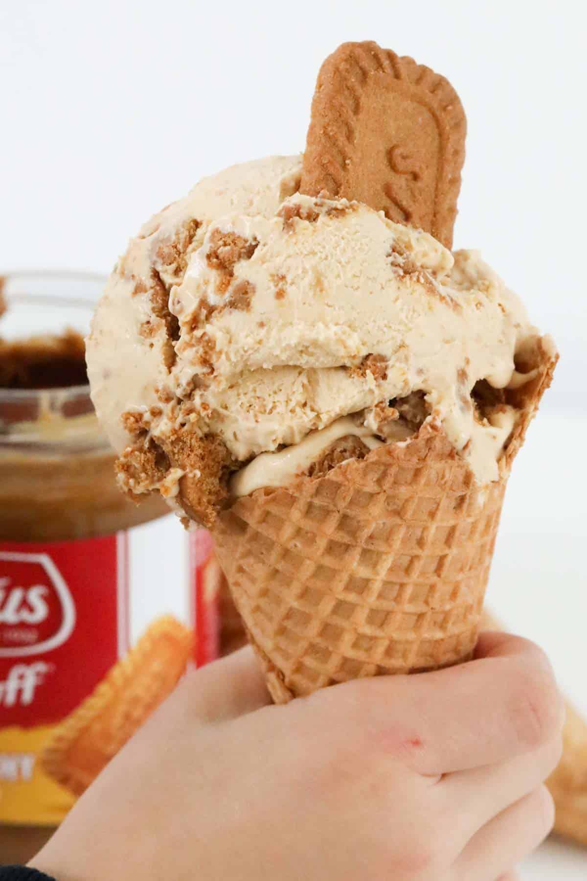 A waffle cone being held, with a Lotus biscuit placed in the ice cream.