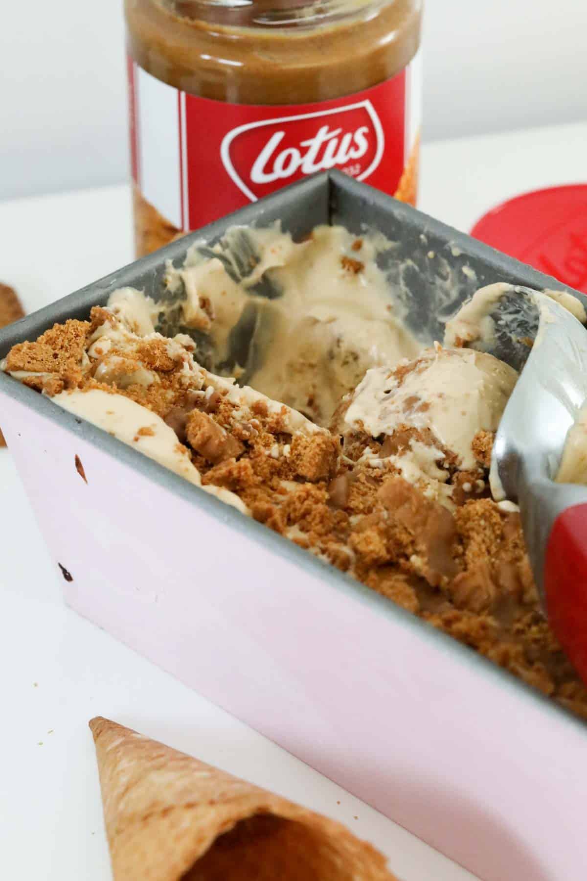 An ice cream scoop rolling a ball of ice cream in a tray of crunchy Biscoff ice cream.