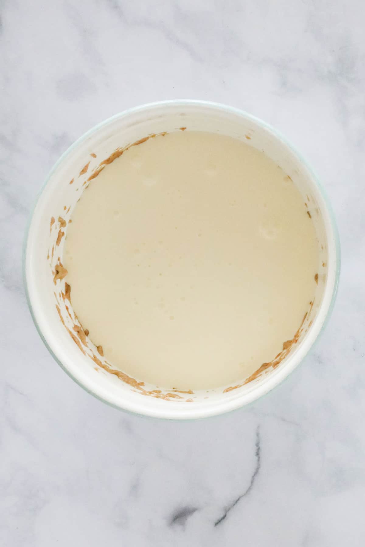 Cream poured into caramel mixture in a white mixing bowl.
