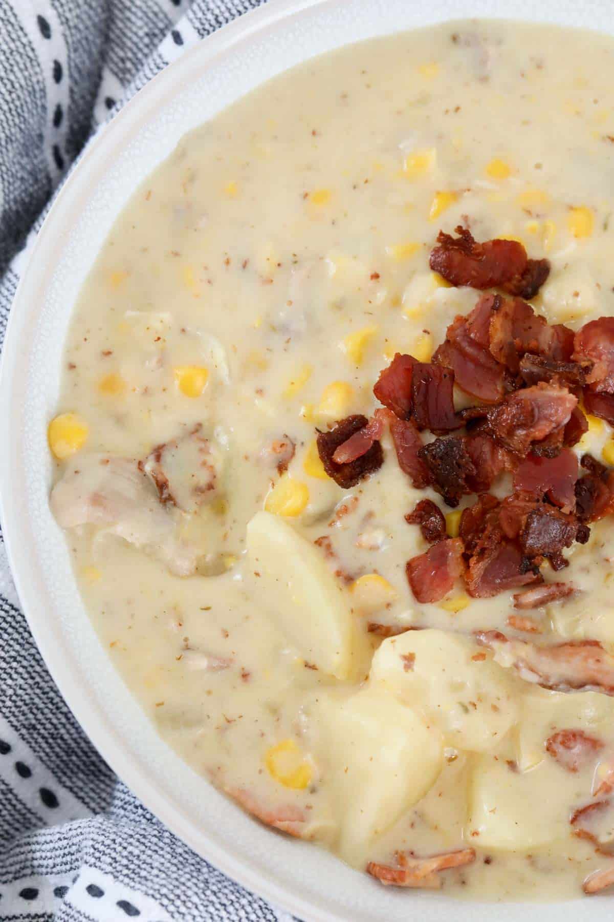 A close up of a bowl of creamy chicken corn soup with crispy bacon sprinkled on top to serve.