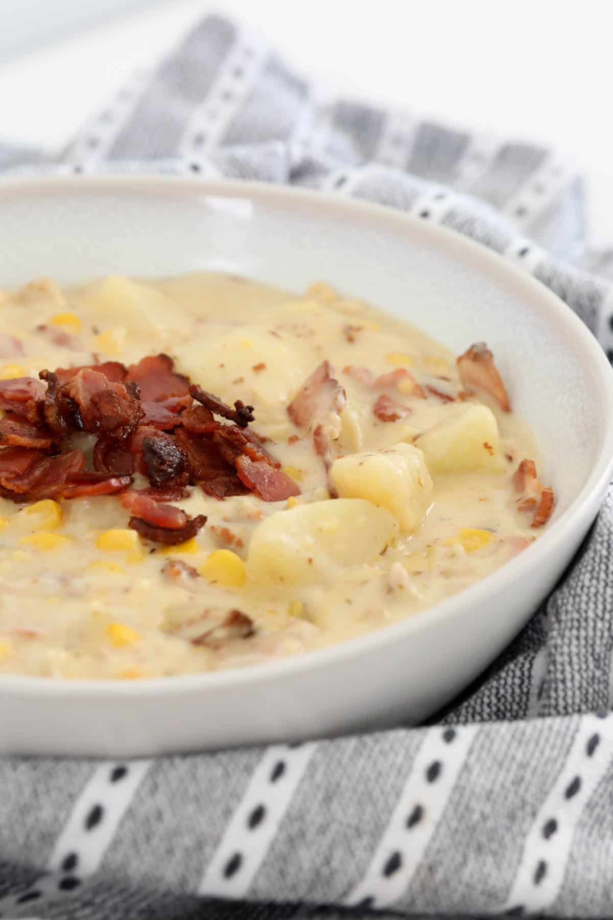 A side view of creamy chicken corn soup in a bowl topped with crispy bacon.