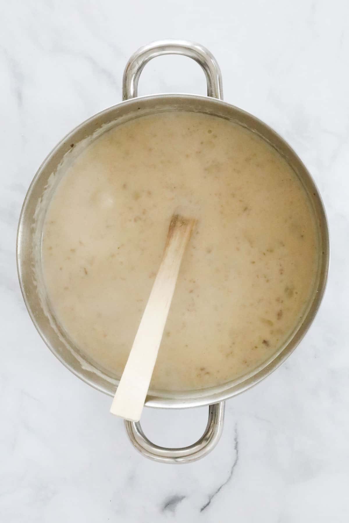 Thick creamy soup base in a saucepan with a wooden spoon.
