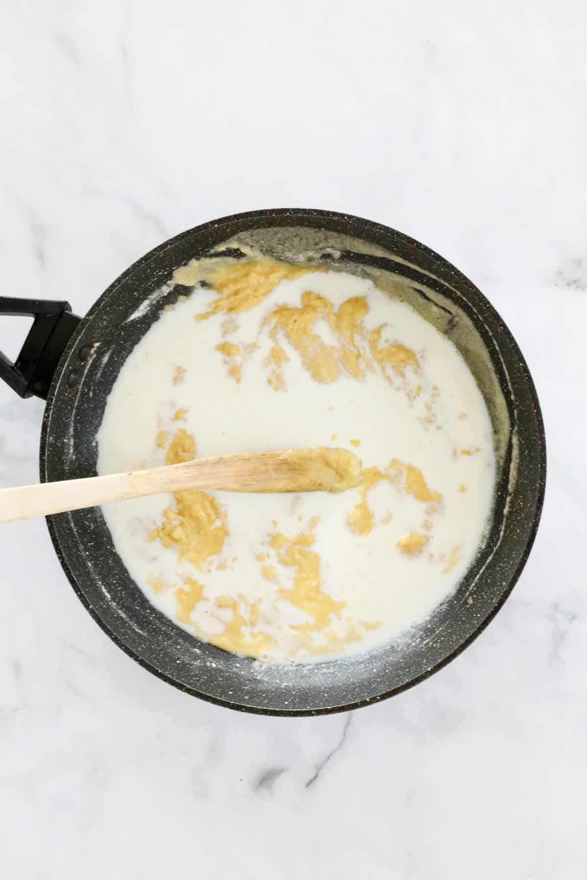 Slowly adding milk to the pan to make creamy cheese sauce.