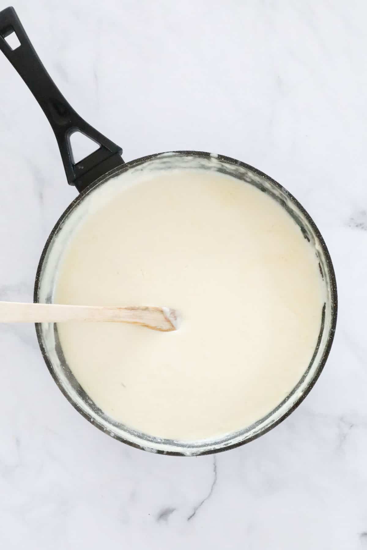 Smooth cheesy sauce with a wooden spoon in a pan.