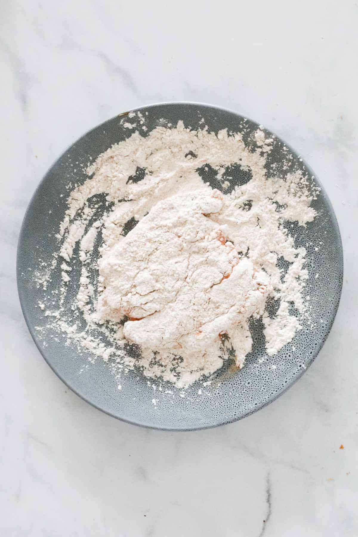 A chicken fillet being tossed in flour.