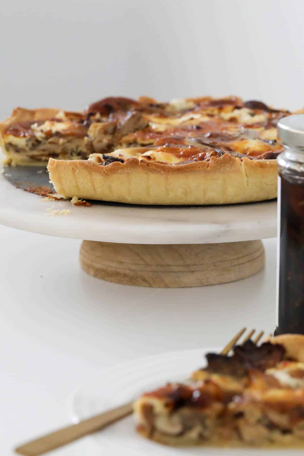A mushroom tart with one serve removed, placed on a cake stand.