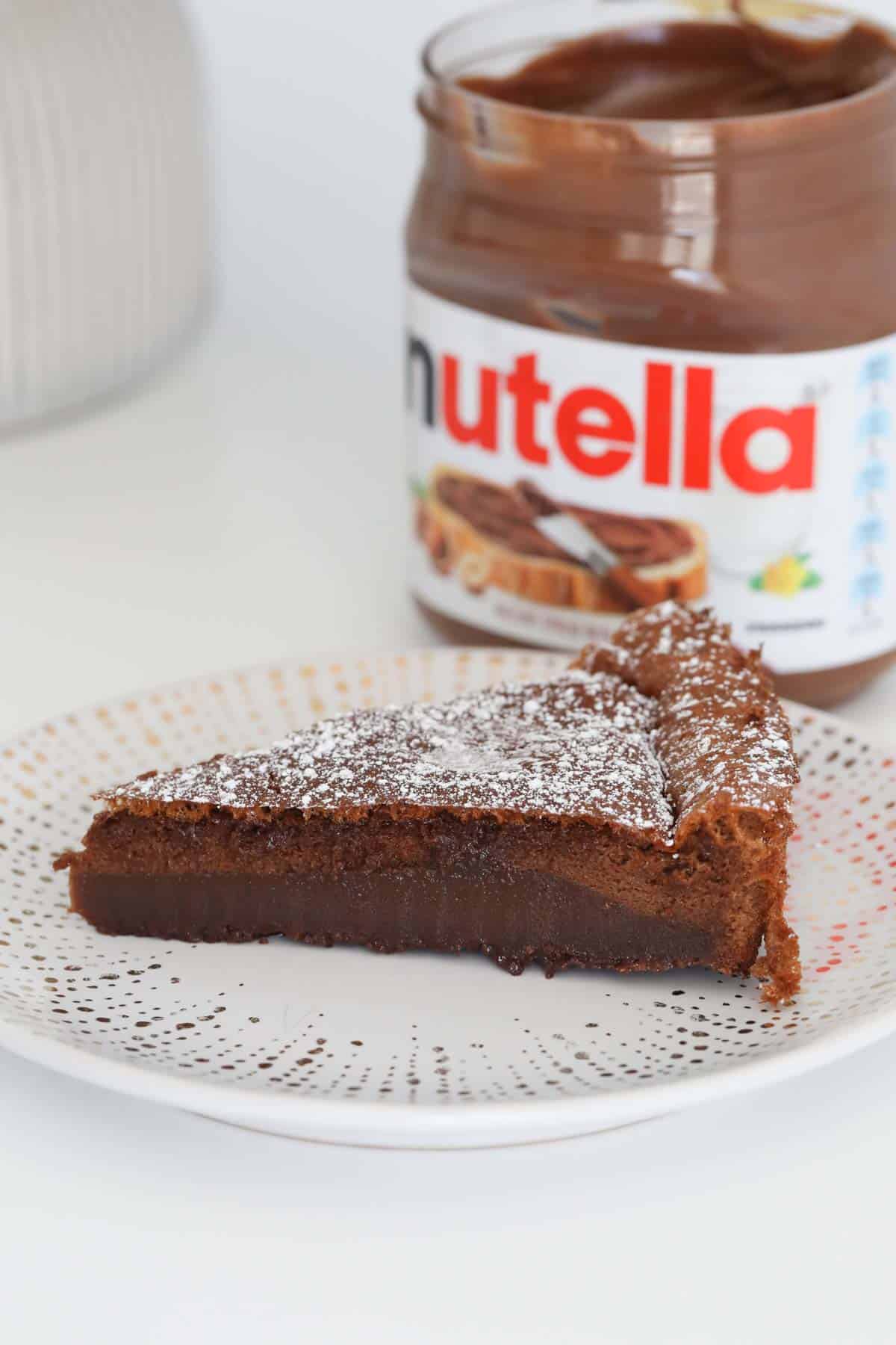 A slice of Nutella cake on a plate with a jar of Nutella just visible behind.