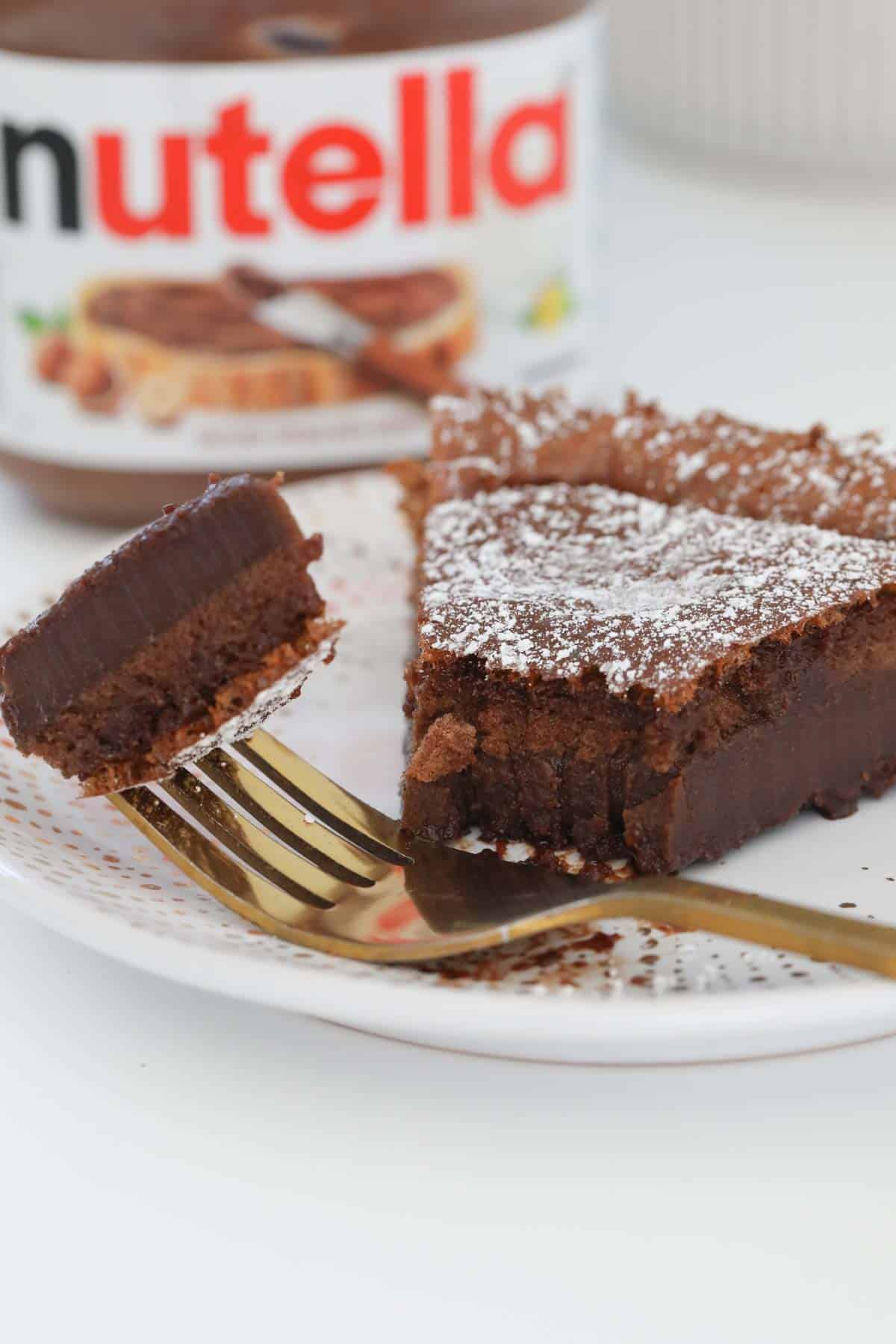 Slice of rich fudgy cake on a plate with a fork holding a mouthful of the cake.