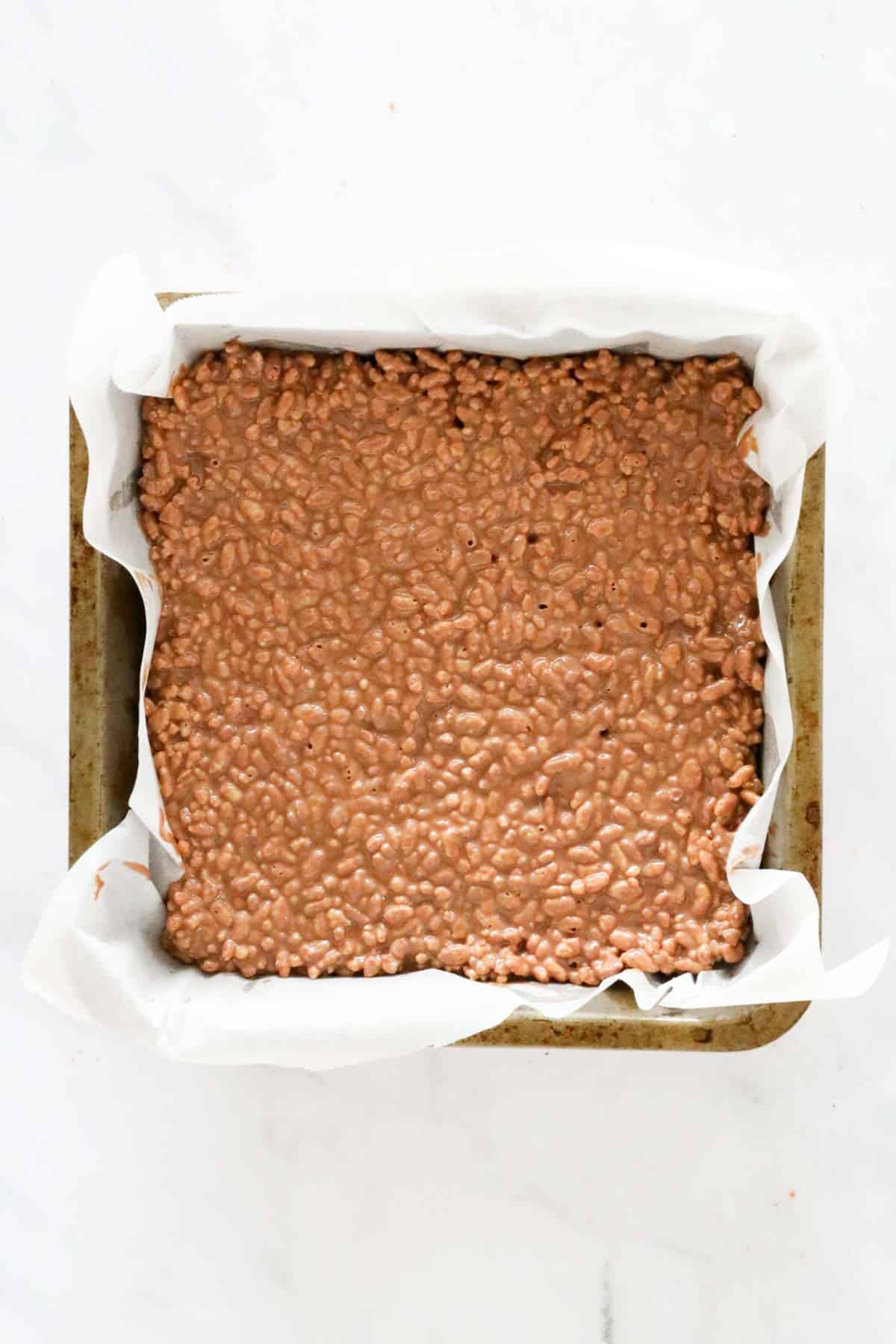 An overhead shot of chocolate peanut butter slice pressed into a paper lined tin.
