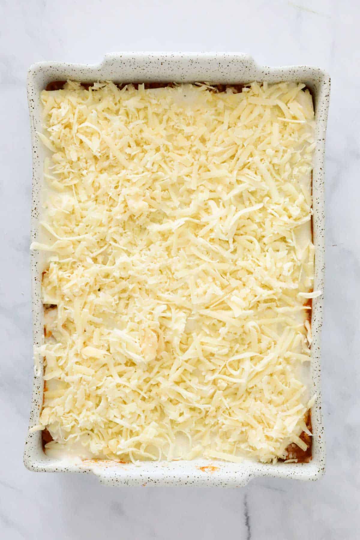 Bechamel sauce and grated cheese sprinkled over a baking dish.
