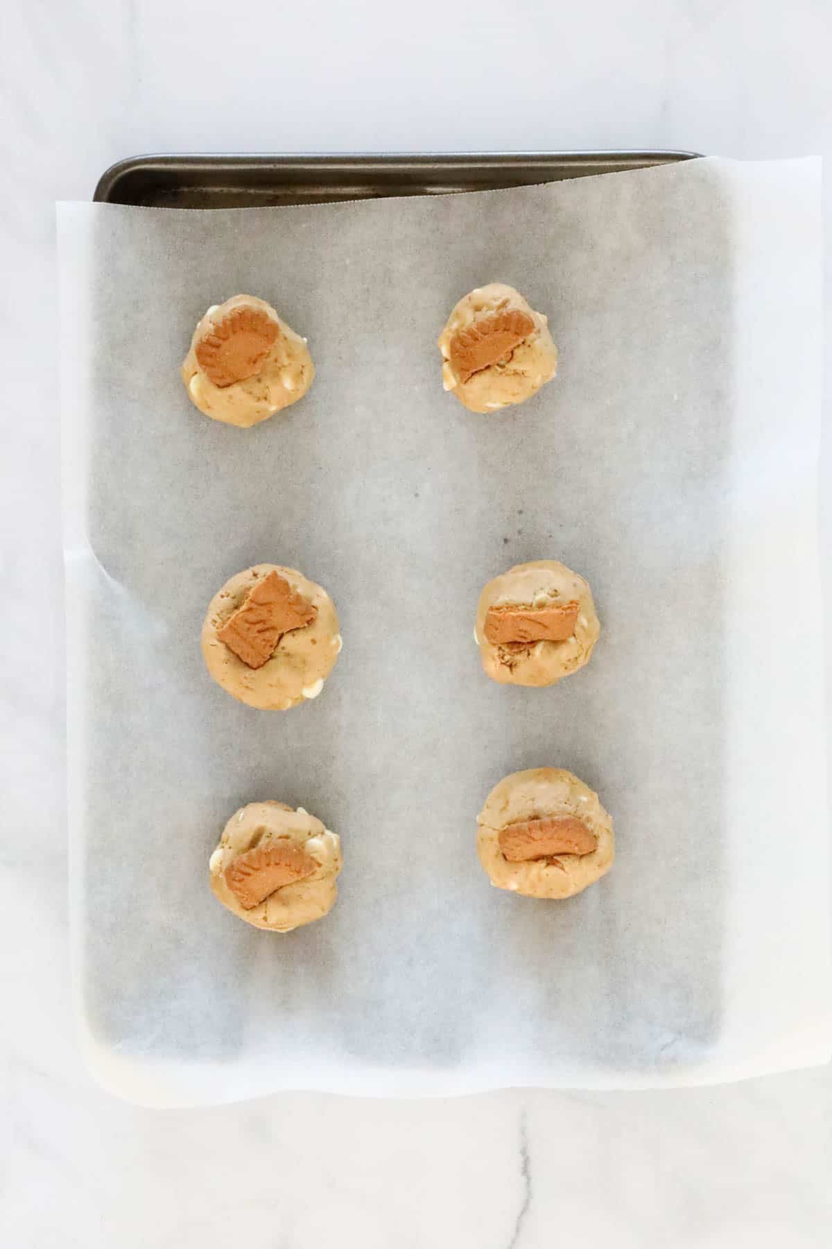 Dough balls placed on baking tray with a piece of Biscoff cookie pressed into the top.