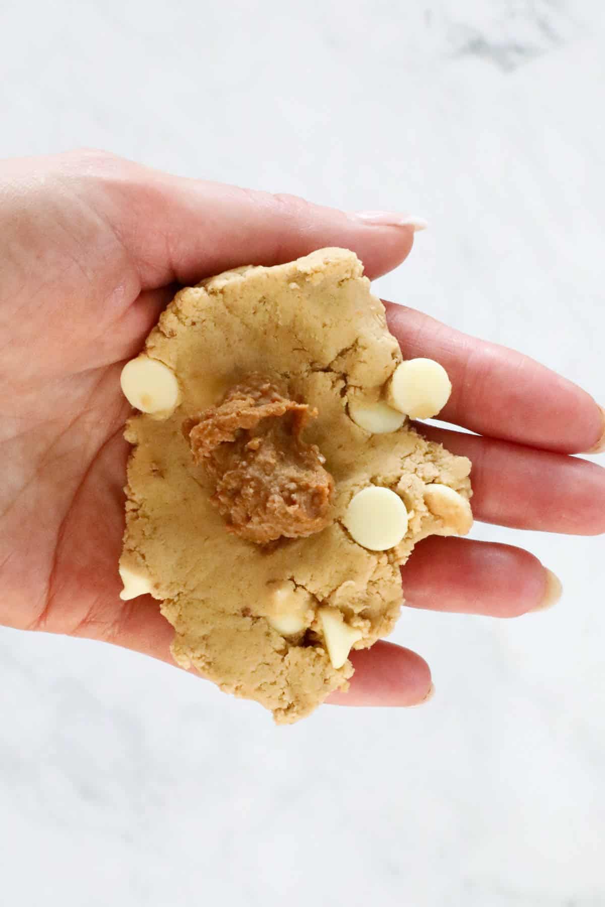 Cookie dough flattened on a palm of a hand, with a small piece of frozen Biscoff spread in the centre.